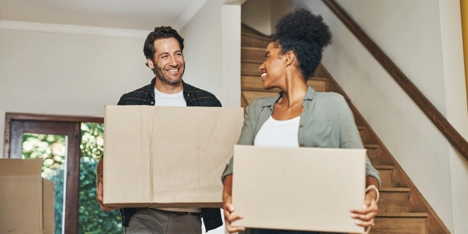 A couple holding moving boxes.