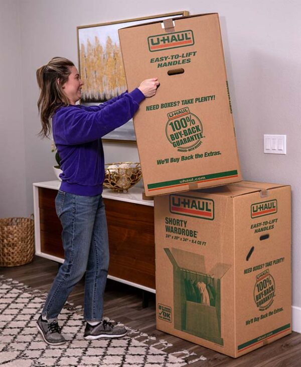 A woman stacks a wardrobe box onto another wardrobe box using the easy-to-lift U-Haul moving boxes