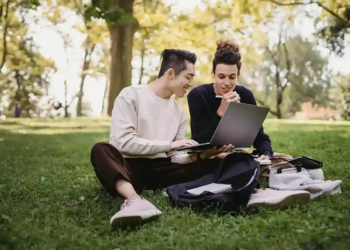 university students in the grass reading a laptop