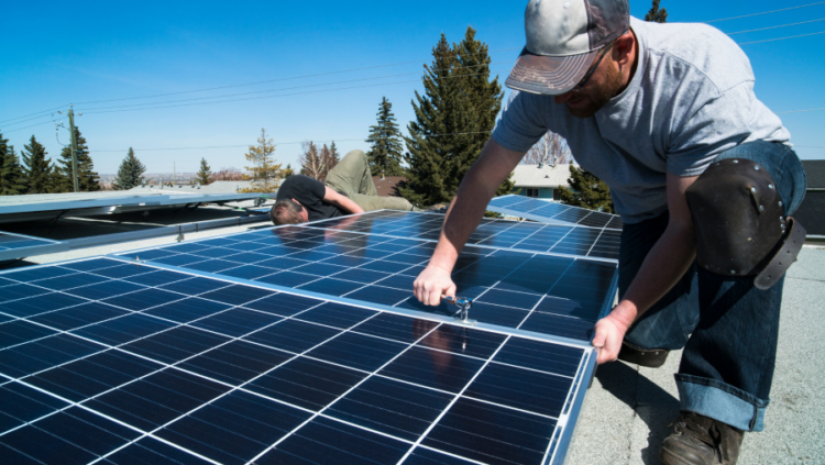 Two people installing a solar panel on a rooftop.