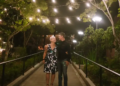 A couple walks hand in hand along a path illuminated by string lights.