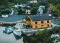 A yellow house by the water, next to a wooden dock, surrounded by a serene landscape.