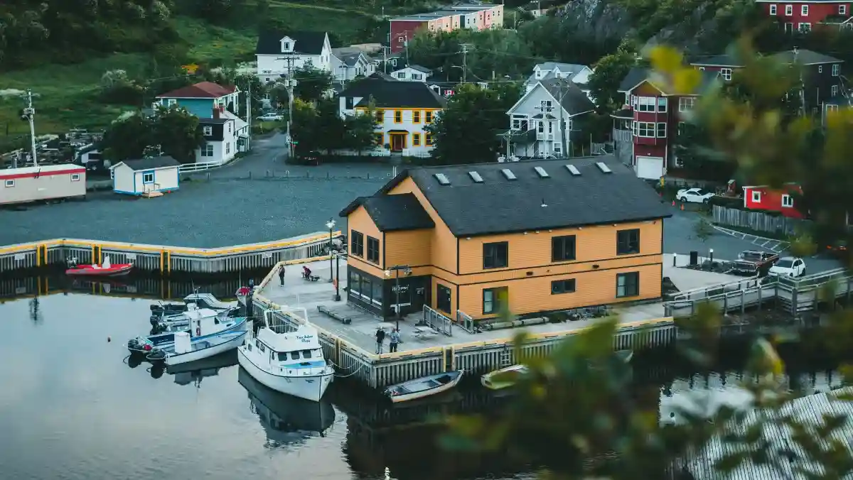 A yellow house by the water, next to a wooden dock, surrounded by a serene landscape.