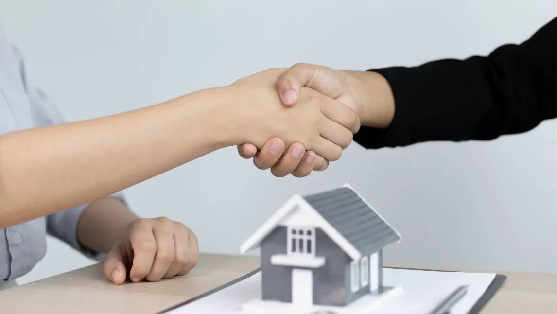 Two people shaking hands over a tiny house model