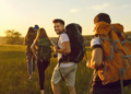 A group of people with backpacks walking through a green field under a clear blue sky.