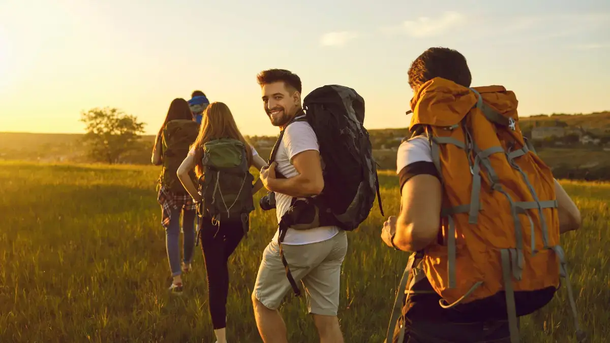 A group of people with backpacks walking through a green field under a clear blue sky.
