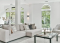 A spacious living room with stylish white furniture and large arched windows.