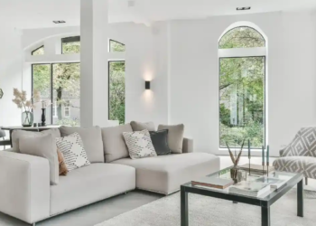 A spacious living room with stylish white furniture and large arched windows.