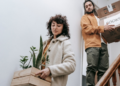 Two people carrying moving boxes down the stairs as they move out of their home.