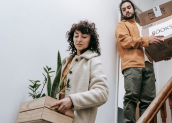 Two people carrying moving boxes down the stairs as they move out of their home.