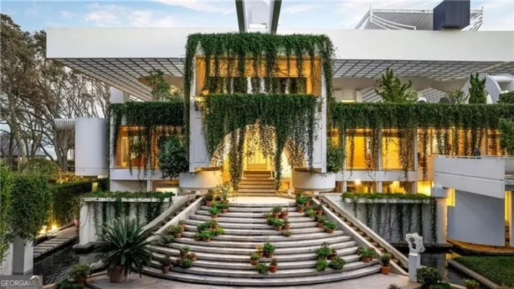 Modern home entrance featuring a large staircase leading up to the front door surrounded by lush greenery.