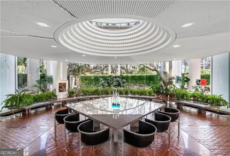 A large room featuring a skylight, a circular table and various plants.