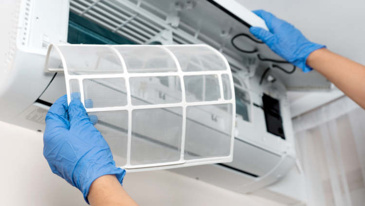 A person wearing blue gloves is holding a window air conditioner, preparing to install it in a home setting.
