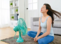 A woman seated on the floor with a fan beside her.