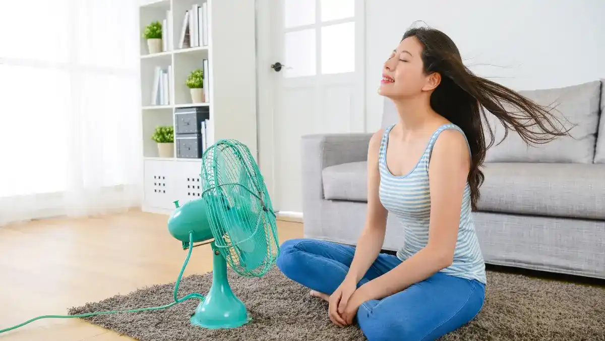 A woman seated on the floor with a fan beside her.