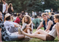 Attendees relax on the grass at a vibrant music festival, engaging with friends and enjoying the lively atmosphere.