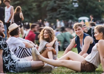 Attendees relax on the grass at a vibrant music festival, engaging with friends and enjoying the lively atmosphere.