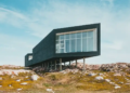 A black house perched on a rocky hill, surrounded by a clear blue sky and distant mountains.