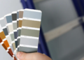 A person holds a paint sample while standing in front of a ladder, preparing for a painting project.