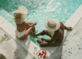 Two people relax in a pool, one wearing a straw hat, enjoying a sunny day together.