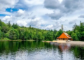 A rustic cabin overlooks a serene lake, surrounded by trees and reflecting the calm water.