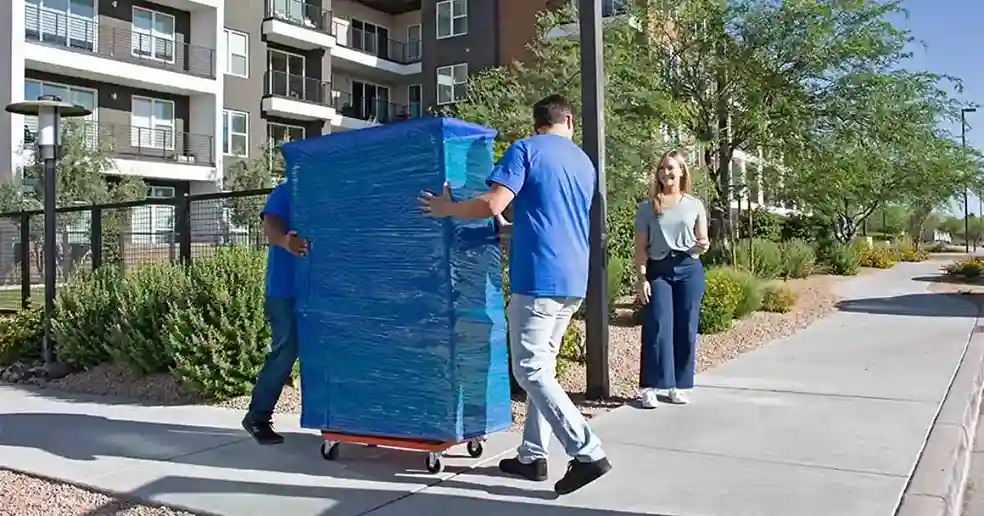 A female customer watches two male providers move a piece of furniture on a furniture dolly.