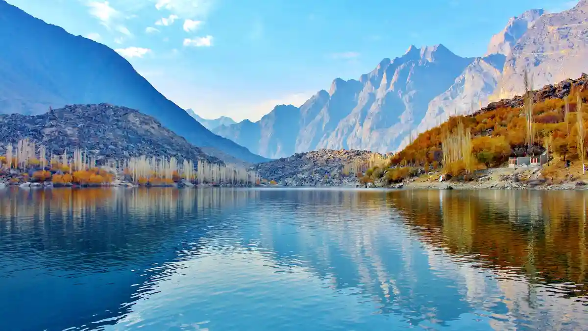 A serene lake nestled among towering mountains and lush green trees under a clear blue sky.