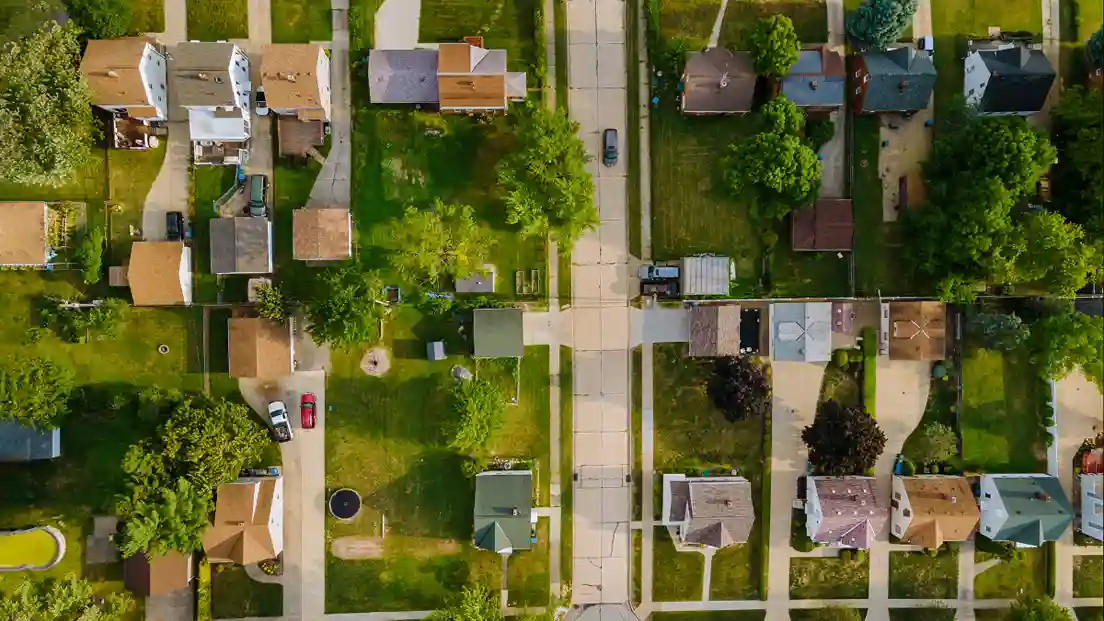 Aerial view of a suburban neighborhood featuring rows of houses with green lawns and tree-lined streets.