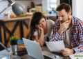 A couple looks stressed while reviewing their finances at the kitchen table.
