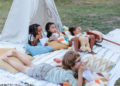 A group of kids having fun on the grass beside a vibrant teepee.