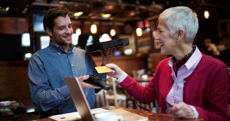 A waiter holds a contactless payment reader as a woman taps her credit card.