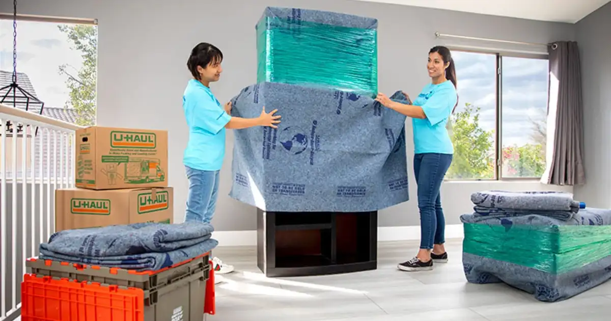 Two Moving Helpers use furniture blankets to wrap a piece of furniture before loading it for a customer.