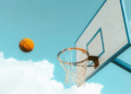 A basketball soaring in the sky towards a basketball net.