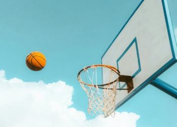 A basketball soaring in the sky towards a basketball net.
