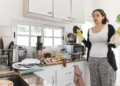 A woman holds cleaning supplies in a dirty kitchen