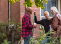 Three neighbors stand in a yard talking to each other