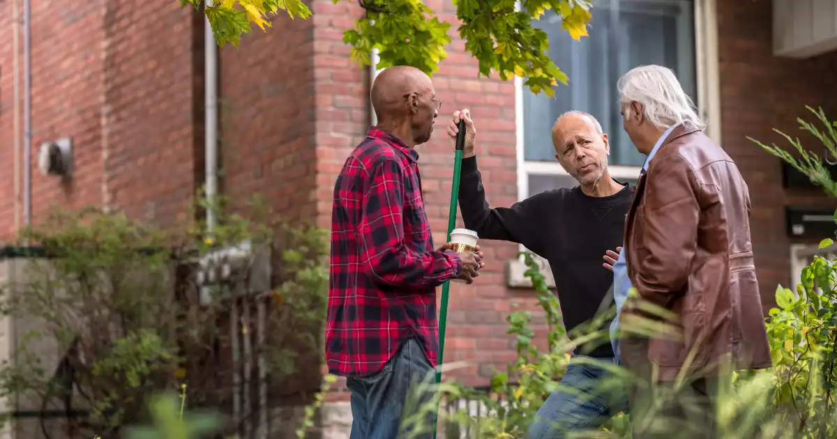 Three neighbors stand in a yard talking to each other