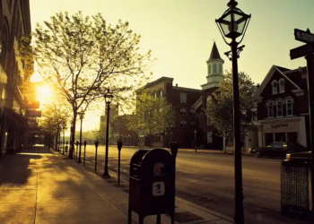 A street lamp illuminating a sidewalk at dusk, casting a warm glow on the surrounding area.