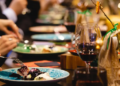 Diners enjoying a meal at a restaurant, with wine glasses and plates on the table, creating a lively dining atmosphere.