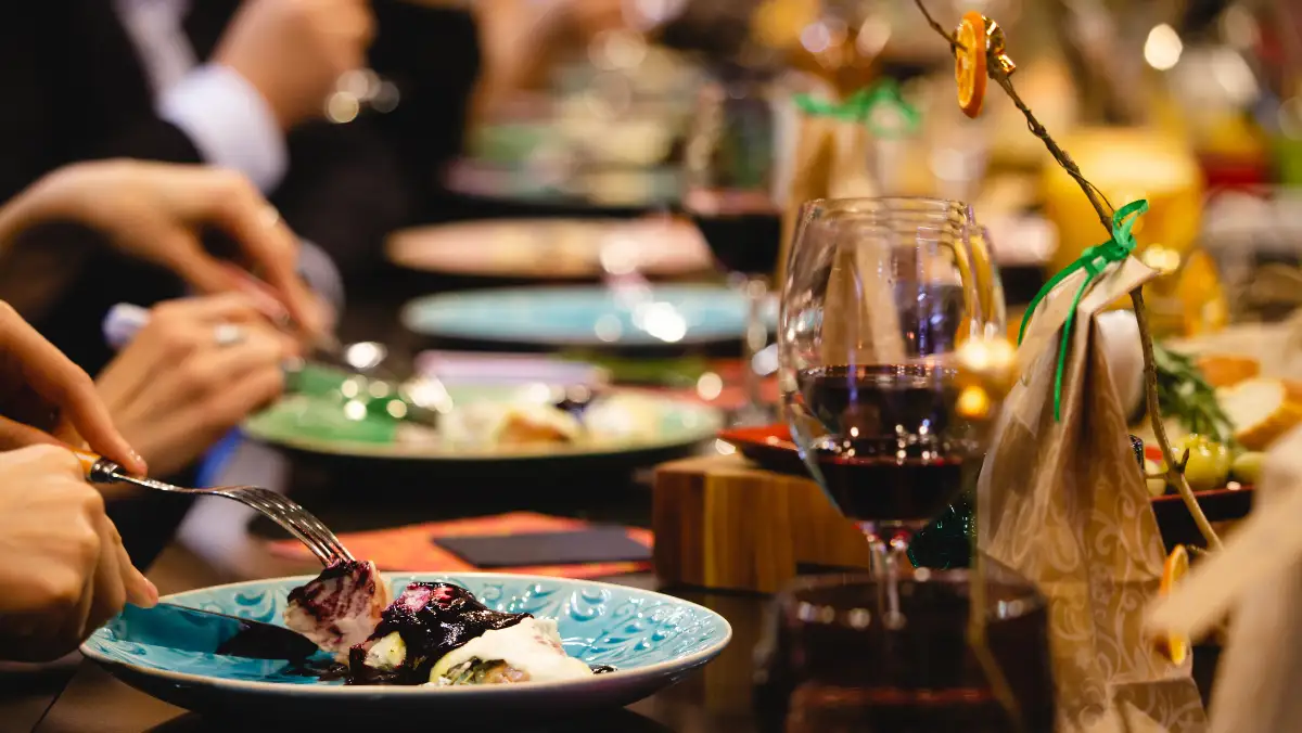 Diners enjoying a meal at a restaurant, with wine glasses and plates on the table, creating a lively dining atmosphere.