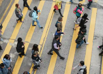 Aerial view of a busy city crosswalk with diverse people crossing in different directions. Yellow stripes highlight the lanes, and the scene feels dynamic.