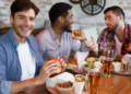 Three friends enjoying a meal at a restaurant, laughing and chatting. Burgers, fries, and beer are on the table. The atmosphere is lively and cheerful.