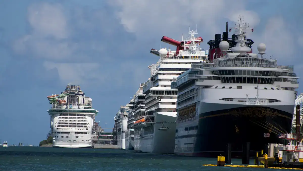 Several large cruise ships docked at a port under a partly cloudy sky. The ships are lined up side by side, creating a sense of grandeur and anticipation.
