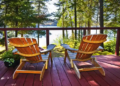 Two wooden chairs sit on a red deck overlooking a serene lake. Surrounded by lush trees, the scene conveys tranquility and natural beauty.