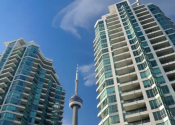 Two modern high-rise buildings with glass facades frame the CN Tower under a clear blue sky, creating an urban skyline scene in Toronto.
