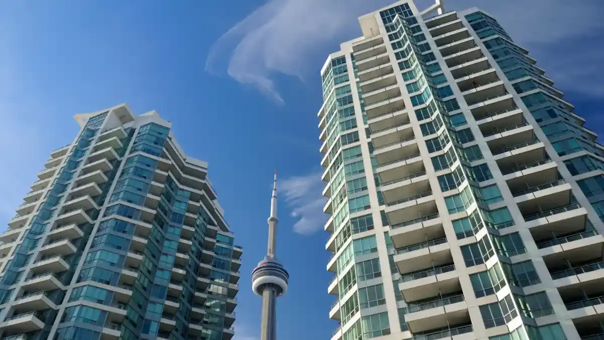 Two modern high-rise buildings with glass facades frame the CN Tower under a clear blue sky, creating an urban skyline scene in Toronto.