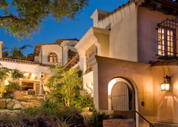 Luxurious Mediterranean-style villa at dusk, lit warmly with lanterns. Features arched doorways, ornate windows, and lush greenery creating an inviting ambiance.